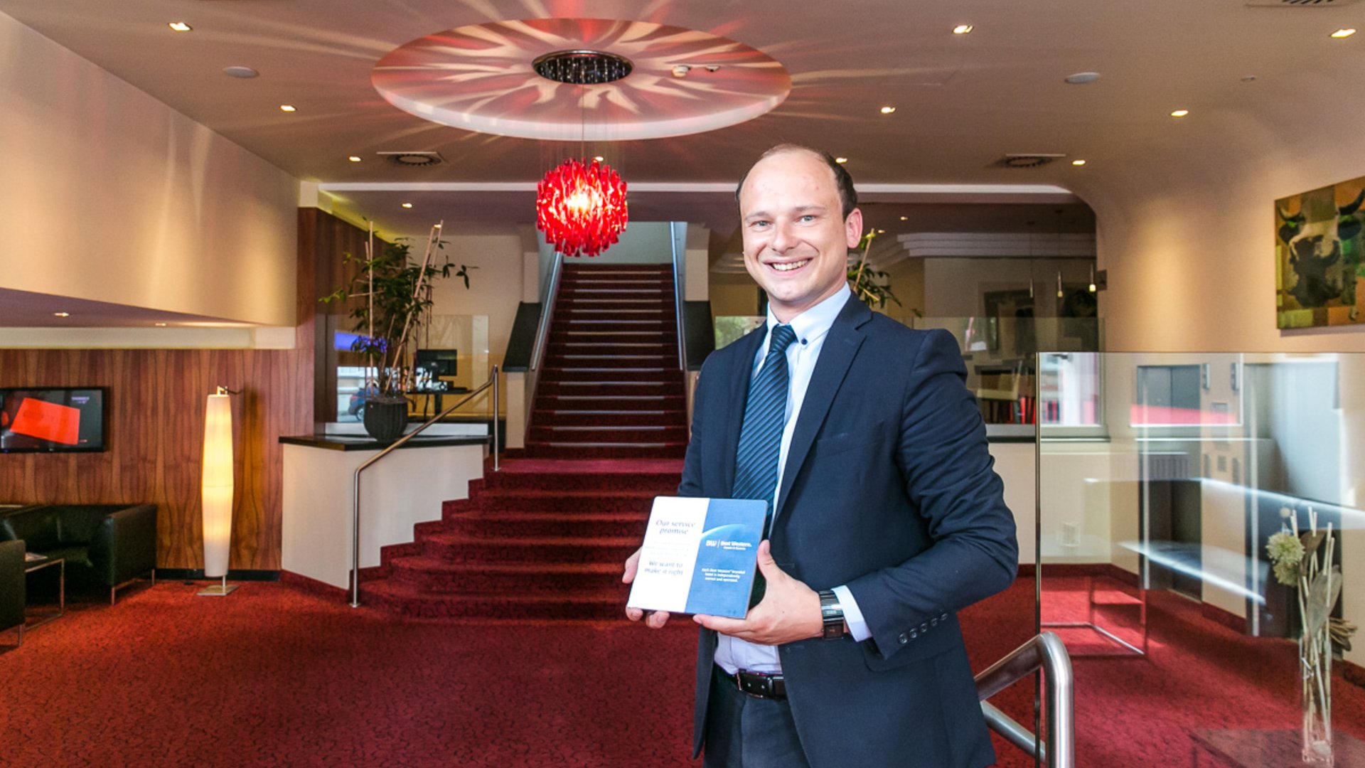 Foto: Fotostudio Eder Linz: Fotografie Julia Mühlberger, Bildbearbeitung Ella Kronberger: Dietmar Pawel Best Western Amedia Wels Hotelmanager Dietmar Pawel präsentiert in der Lobby stehend eine Bonuskarte.