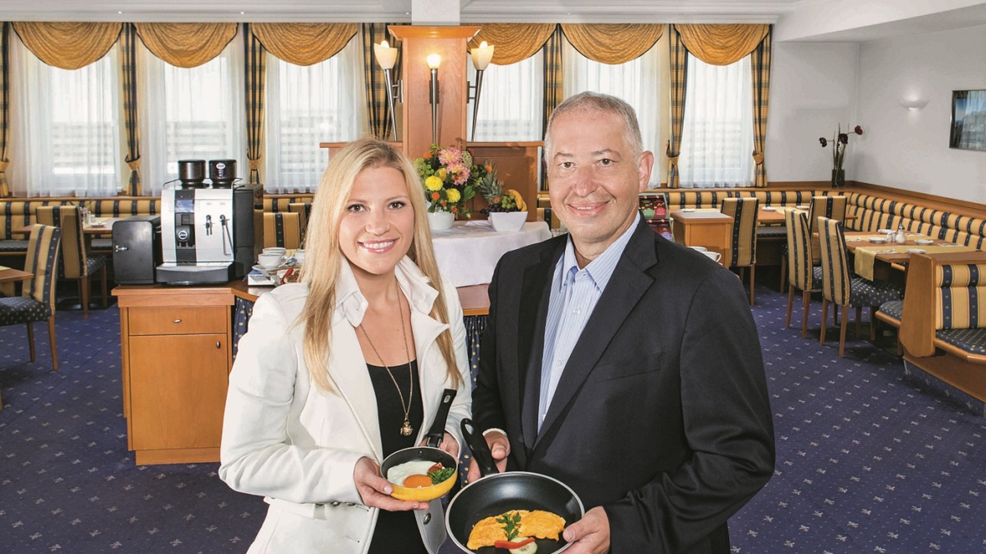 Foto: Fotograf Eder Linz Fotografie Julia Mühlberger, Bildbearbeitung Ella Kronberger: Alexandra und Helmut Platzer Hotel Alexandra und Bayrischer Hof, Alexandra und Helmut Platzer Der Hotelier Helmut Platzer steht neben seiner Tochter Alexandra im Frühstücksraum, beide präsentieren ein Spieglei in der Pfanne.